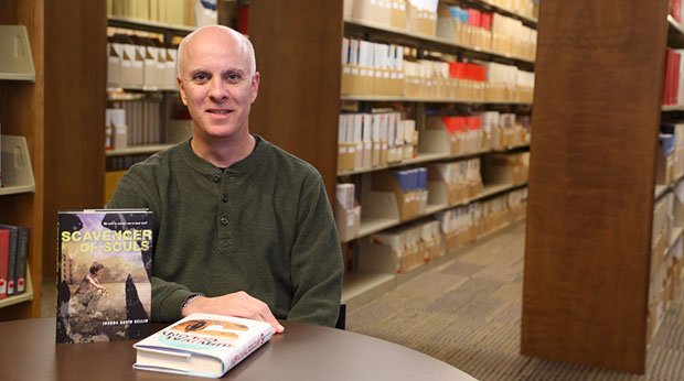 Professor Dr. Joshua Bellin poses with his two science fiction novels in the Wright Library at La Roche University.